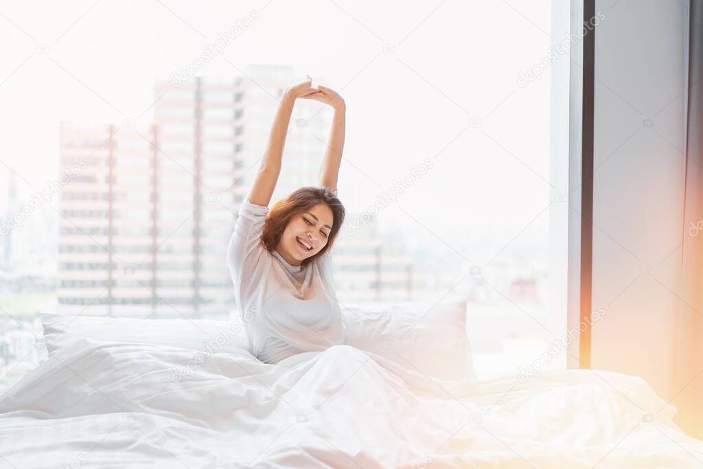 Wake up scene of young woman in bright morning with fresh and relaxation day. comfortable lifestyle in the bed room with city view at the morning sun light.