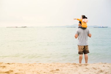 Asyalı baba ve kızı haftasonu kumsalda birlikte vakit geçirirken küçük kız elini gökyüzüne doğru tutuyor. Aile kumsalda yürüyor, dünya çocuk deneyimini keşfediyor.