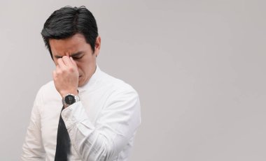 Yorgun Asyalı bir işçinin kaşlarının arasına sıkıştırıp sıkı çalışmayı denemesi acı ifadesi ifadesi, bitkin çalışma konsepti, ofis çalışanı yaşam tarzı, ofis sendromu, yorucu çalışma saati..