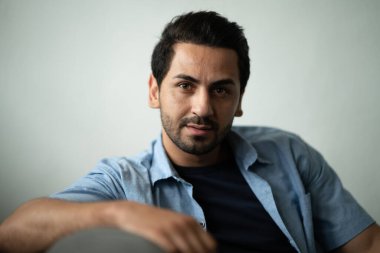 İspanyol yakışıklı sakallı adamın portresi, güneş ışığı odasındaki kameraya bakarken koltukta otururken ciddi görünüyor..