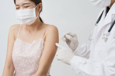 Profesyonel doktor ya da hemşire, koruyucu maske takan hasta kadın için şırınga aşısı kullanıyor. Aşı ve aşı kampanyası sırasında Asyalı kız hastanede ya da sağlık merkezinde aşı oluyor..