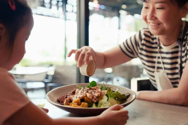 Mutlu Asyalı aile. Anne ve kızı restoranda sağlıklı salata yiyorlar. Salata tabağına odaklan.