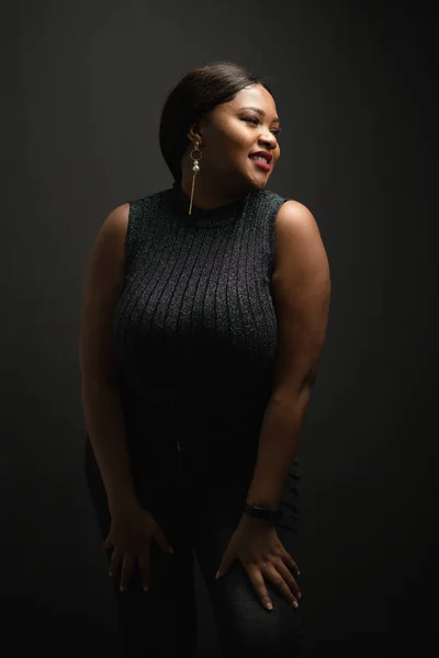 Portrait of black woman plus size smiling with confident and looking toward to camera in the dark background.