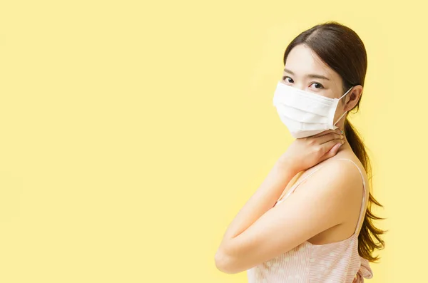 Asian woman wearing a surgical face mask and turn her face to camera over yellow background.