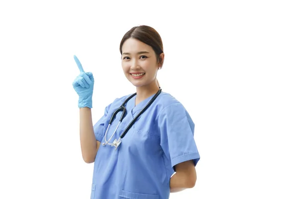 若いですアジアの女性で看護師の制服で聴診器と身に着けています青ニトリル手袋ポイント彼女の指左画面にコピースペースを持っています 隔離された白い背景に概念看護師発表者 — ストック写真