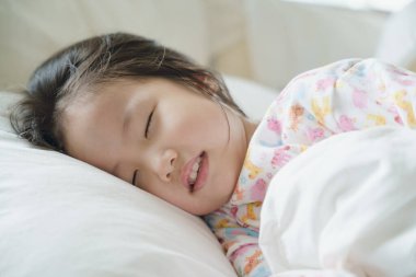 Sabahın ilk ışıklarıyla yatağında uyuyan çocuk sahnesi. Asyalı küçük kız uyuyor..