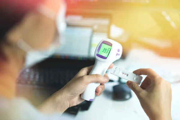 Yüksek ateş ve kovid 19 için antijen hızlı test kiti streptokok gösteren kızılötesi termometreyi tutan elleri kapatın. Belirtileri olduğunda evde kendini kontrol et