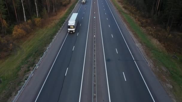 Samochody i ciężarówki jadą po pustej autostradzie wzdłuż jesiennego lasu — Wideo stockowe