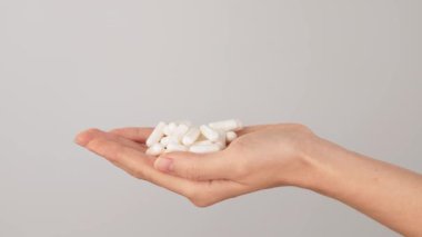Tarafsız bir arkaplanda fotokopi alanı olan bir yığın beyaz kapsülü tutan bir el. Beslenme takviyeleri, vitaminler ve sağlık hapları kavramı.
