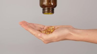Kahverengi bir şişeden dökülen altın yumuşak kapsüllerle dolu bir elin yakın çekimi. Vitamin, balık yağı, omega 3 takviyesi, sağlık hizmetleri ve günlük sağlık rutini kavramı.