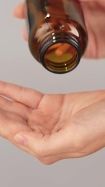 Şişeden dökülen sarı kapsüllerle dolu bir elin dikey yakın çekimi. Vitamin, bitkisel takviye, zerdeçal kömür, ilaç ve günlük sağlık hizmetleri kavramı.