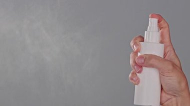 Tarafsız bir arkaplanda beyaz bir şişeden ince bir sis püskürten bir elin yakın çekimi. Saç spreyi ya da fotokopi alanında kullanılan ısı koruması. Saç bakımı