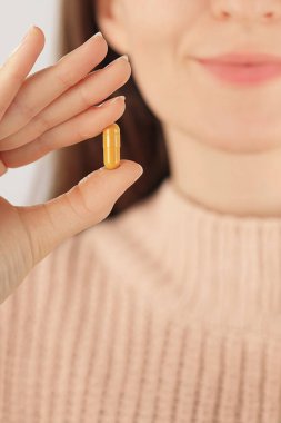 Sarı bir kapsül tutarken gülümseyen tanınmayan bir kadının yakın çekimi. Bitkisel takviyeler, vitaminler ve günlük sağlık rutini kavramı.