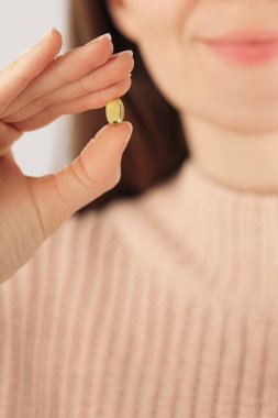 Kolajen kapsül güzellik ilavesi tutan tanınmayan gülümseyen bir kadının yakın çekimi. Cilt bakımı, yaşlanma karşıtı, kişisel bakım ve günlük sağlık rutini kavramı.