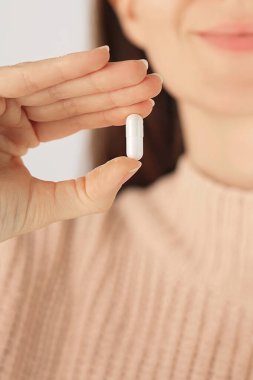 Beyaz kapsül ilacı ya da vitamin içeren bir elin dikey yakın çekimi. Tedavi, önleme ve günlük sağlık rutini kavramı.