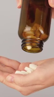 Şişeden dökülen beyaz tabletlerle dolu bir elin dikey yakın çekimi. İlaçlar, multivitaminler, ağrı kesici ve günlük sağlık hizmetleri rutini.