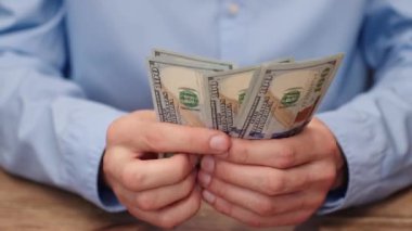 Adam 100 dolarlık banknotları yakından sayıyor. Yatırım veya zenginlik geliştirme, mali planlama veya gelir için yatırımcı kavramı