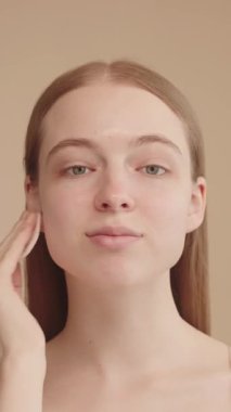 Genç, beyaz bir kadın yüzünü pamukla temizliyor. Temizlik, bakım ve kozmetik için. Doğal güzellik ve cilt rutini. Kameraya bakıyor..