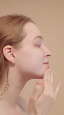 Yüzüne, cildine ve güzellik rutinine nemlendirici sürerek makyaja hazırlanan bir kadının yan görüntüsü. Çekici genç bayan krem sürüyor. Dikey video