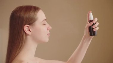 Yüzüne sis şişesi püskürten genç bir kadının yandan görünüşü nemlendiriciyi günlük cilt bakımında nemlendirici olarak kullanıyor..