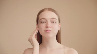 Genç, beyaz bir kadın yüzünü pamukla temizliyor. Temizlik, bakım ve kozmetik için. Doğal güzellik ve cilt rutini. Kameraya bakıyor..