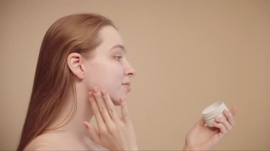 Sabah cilt bakımını yapan genç bir kadın güneş kremi ve makyaj malzemesi sürüyor. Cildi makyaja hazırlıyor. Günlük güzellik rejiminin bir parçası..