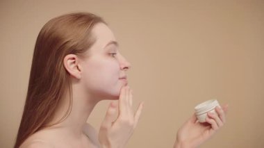 Yüzüne, cildine ve güzellik rutinine nemlendirici sürerek makyaja hazırlanan bir kadının yan görüntüsü. Çekici genç bayan krem sürüyor.