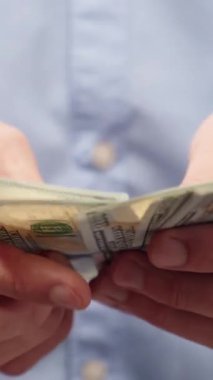 Erkek eli, Amerikan dolarlarını sayıyor. Mavi gömlekli adam para sayıyor, 100 dolarlık banknotlar. Gelir, maaş veya tasarruf planlaması için mali konsept.