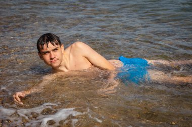 18 yaşında, beyaz tişörtsüz, sörfte yatan genç bir çocuk.