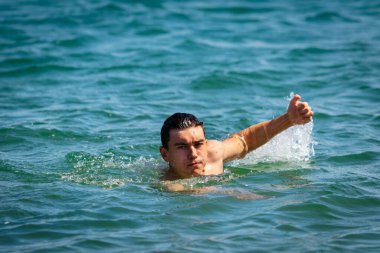 18 yaşında, beyaz, mayo giyen, denizde yüzen genç bir çocuk.