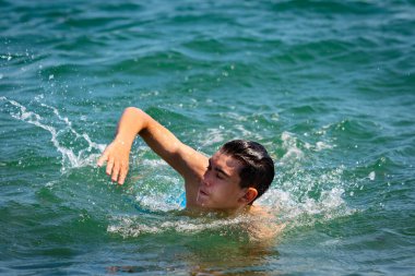 18 yaşında, beyaz, mayo giyen, denizde yüzen genç bir çocuk.