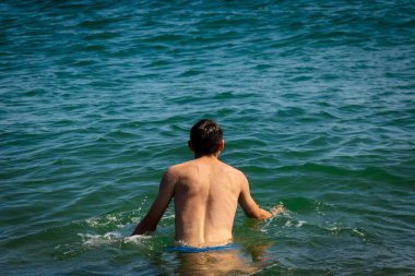 Denizde mayo giyen 18 yaşında, beyaz tişörtsüz bir genç.