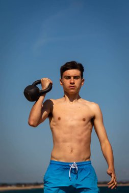 18 yaşında, beyaz, mayo giyen, kettlebell ağırlığıyla egzersiz yapan genç bir çocuk.