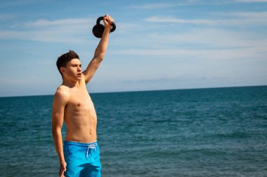 18 yaşında, beyaz tişörtsüz mayo giyen genç bir çocuk. Fotokopi odasıyla kettlebell ağırlığında egzersiz yapıyor.