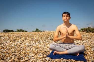 Sahilde fotokopi uzayı ile meditasyon yapan 18 yaşında beyaz bir çocuk.
