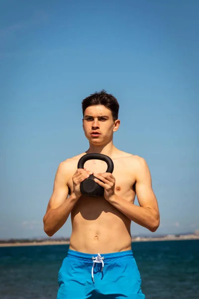 Plajda Kettlebell Ağırlığıyla Egzersiz Yapan Yaşında Beyaz Gömleksiz Bir Genç — Stok fotoğraf