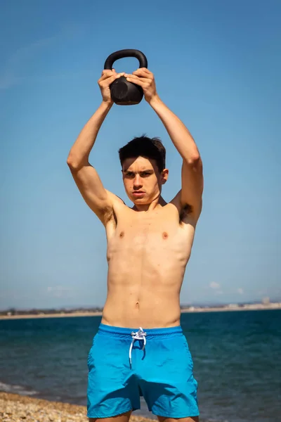 18歳の白人男の子10代の少年ビーチでケトルベルの重さで運動 — ストック写真