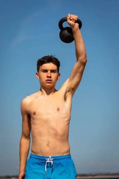 18歳の白人無学の十代の男の子で水着練習でケトルベルの重さ — ストック写真