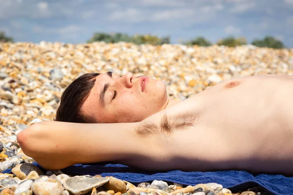 一名18岁的白种人少年赤身裸体在石头砸人的海滩上晒日光浴 — 图库照片