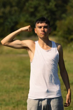 18 yaşında kolsuz tişörtlü bir genç yaz günü kol kaslarını esnetiyor.