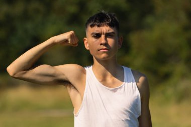 18 yaşında kolsuz tişörtlü bir genç yaz günü kol kaslarını esnetiyor.