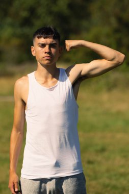 18 yaşında kolsuz tişörtlü bir genç yaz günü kol kaslarını esnetiyor.