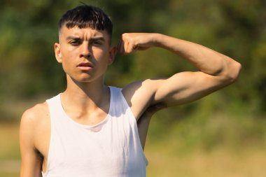 18 yaşında kolsuz tişörtlü bir genç yaz günü kol kaslarını esnetiyor.