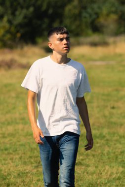18 yaşında, açık havada beyaz tişörtlü ve kot pantolonlu bir çocuk.
