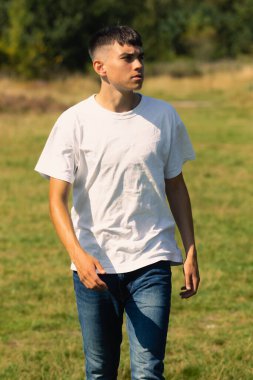 18 yaşında, açık havada beyaz tişörtlü ve kot pantolonlu bir çocuk.