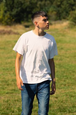 18 yaşında, açık havada beyaz tişörtlü ve kot pantolonlu bir çocuk.