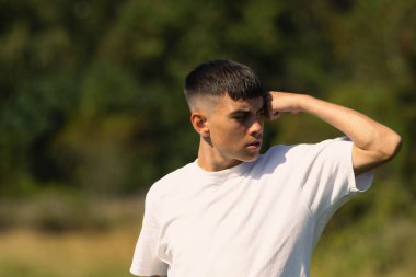 18 yaşında, beyaz tişörtlü, kollarından birini esnetiyor.