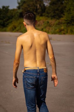 18 yaşında genç bir çocuk sıcak bir yaz gününde kot pantolon ve gömleksiz yürüyor.