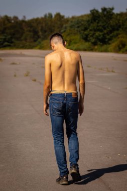 18 yaşında genç bir çocuk sıcak bir yaz gününde kot pantolon ve gömleksiz yürüyor.