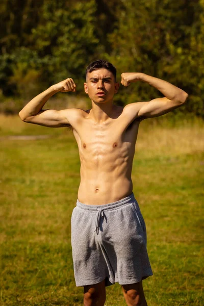 暖かい夏の日に彼の筋肉を曲げ18歳の10代の男の子のショートパンツとシャツを着て — ストック写真
